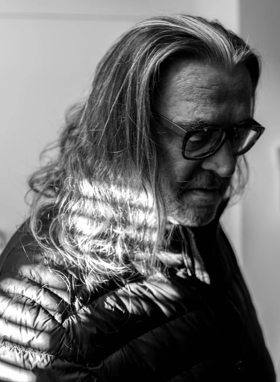 Black-and-white portrait of a person with glasses, with striped sunlight falling across their face and clothing.