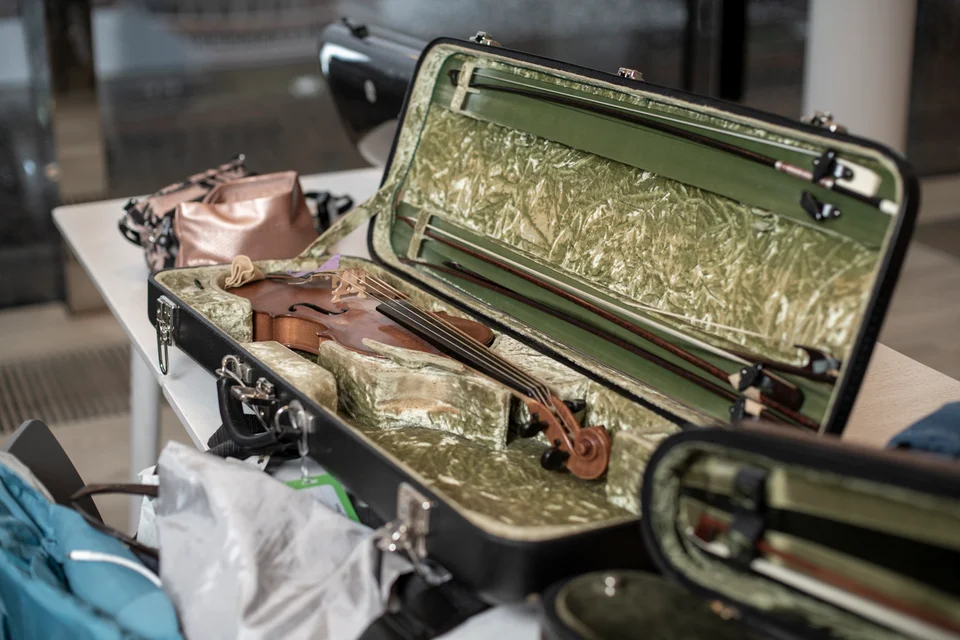 A violin resting in an open, green-lined case among other instrument cases.